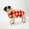 Pug wearing an orange check Fleece Dog Coat on a white background.