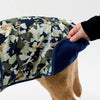 Camouflage-patterned dog coat being held by a person on a white background