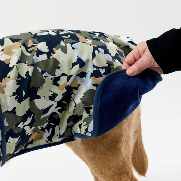 Camouflage-patterned dog coat being held by a person on a white background