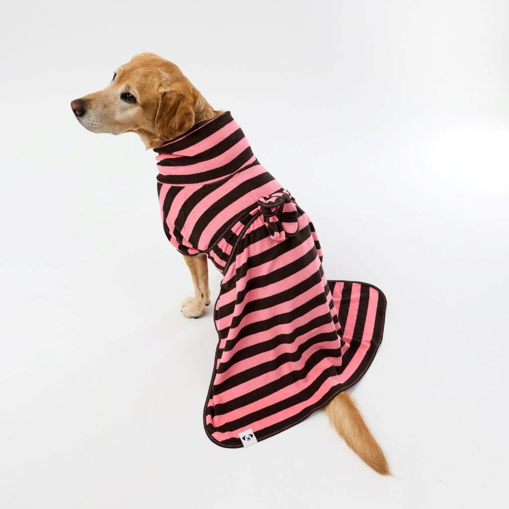 A golden retriever dog wearing a pink and chocolate striped dog towel robe, photographed against a seamless white studio background.
