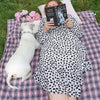 A lady reading a book is lying with her dog on a pink check fleece blanket.