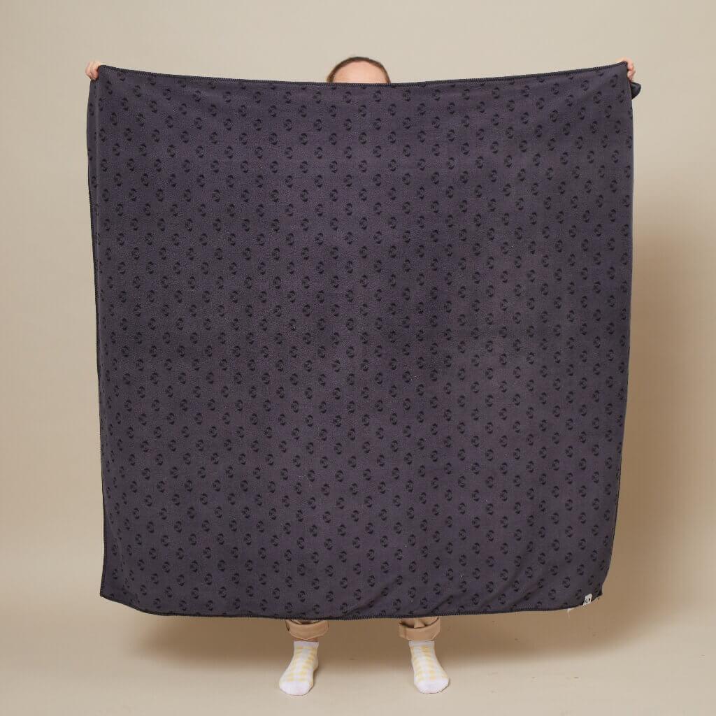 A person holding up a fleece blanket to show the size of it unfolded.